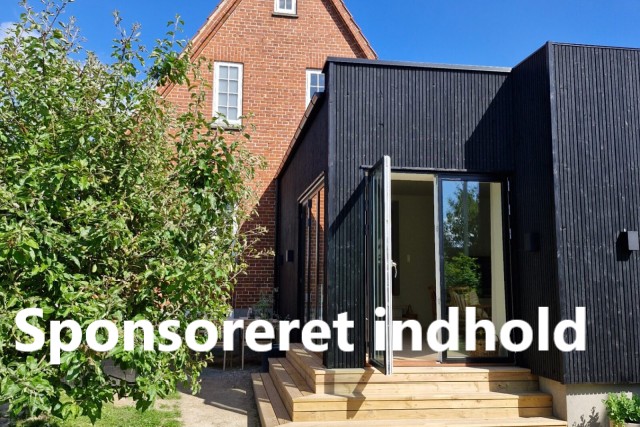 Tilbygning med sort træbeklædning bygget til et rødt murstenshus